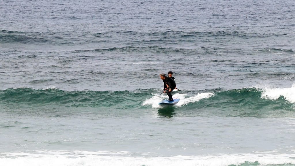 SUP_surfing001 | 奄美大島サーフィンスクールと体験、 サップ体験とシュノーケルツアーKazbo Two people surfing on a blue board on a small ocean wave near the shore